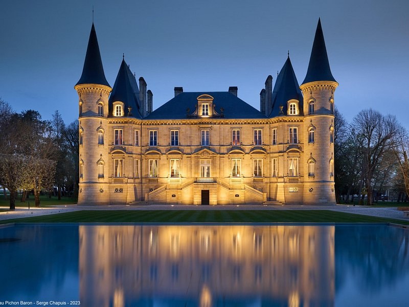 Château Pichon Baron lit at dusk, its turrets mirrored in the pool in front