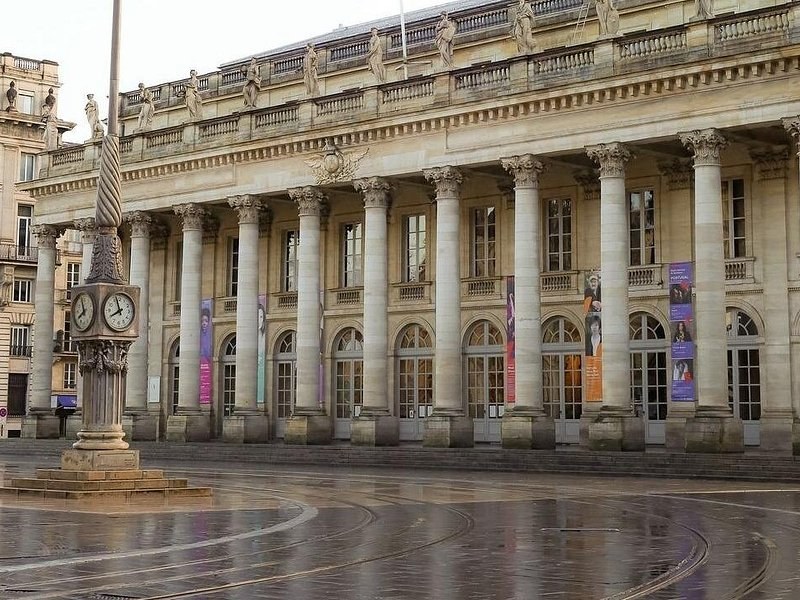 The columned portico of the Grand Théâtre, statues along its roofline, on a wet morning
